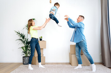 Young parents play with their little beautiful son, they throw him to each other, the son is very...