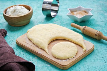Step by step preparation of yeast donuts on a turquoise concrete background. Step One, rolling dough and cutting donuts with round cutting