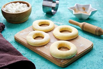 Step by step preparation of yeast donuts on a turquoise concrete background. Step Three, formed donuts with proofers before deep-fried.