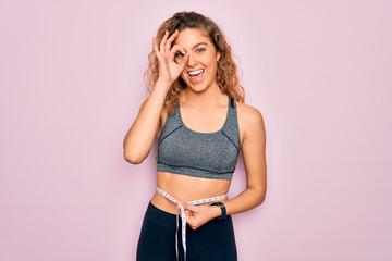 Young blonde sporty woman with blue eyes controlling weight using tape measure on waist with happy...