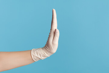 Profile side view closeup of human hand in white surgical gloves showing stop with hand. indoor,...