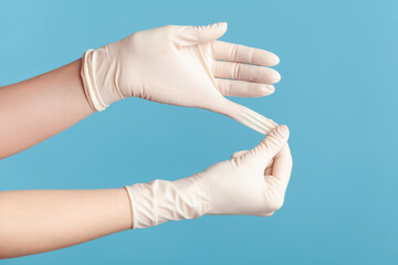 Profile side view closeup of human hand in white surgical gloves showing how to take of gloves. indoor, studio shot, isolated on blue background.