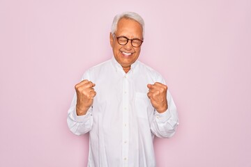 Middle age senior grey-haired man wearing glasses and business shirt over pink background very happy and excited doing winner gesture with arms raised, smiling and screaming for success. Celebration