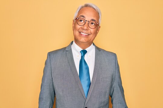 Middle age senior grey-haired handsome business man wearing glasses over yellow background smiling looking to the side and staring away thinking.