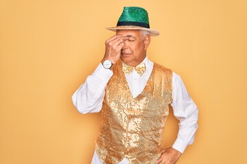 Middle age senior grey-haired man wearing Brazilian carnival custome over yellow background tired rubbing nose and eyes feeling fatigue and headache. Stress and frustration concept.