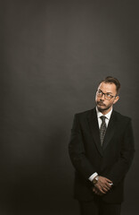 Thoughtful businessman waits standing with clasped hands and looking up against gray wall back. Template for business ideas, schemes and diagrams. Background for creativity and sketches. Toned image.