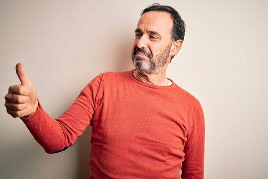 Middle age hoary man wearing casual orange sweater standing over isolated white background Looking proud, smiling doing thumbs up gesture to the side
