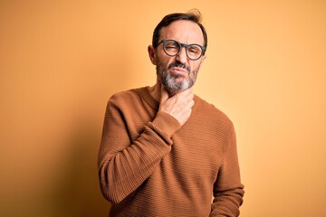 Fototapeta premium Middle age hoary man wearing brown sweater and glasses over isolated yellow background Touching painful neck, sore throat for flu, clod and infection