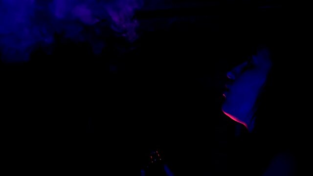 Silhouette of young woman smoking vape on the black background at nightclub