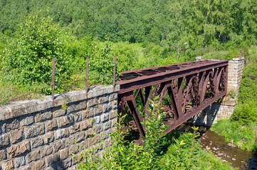 Old rusty inactive railway bridge on the Circum-Baikal Railway densely overgrown with trees