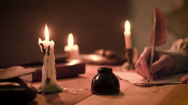 Scene from the 18th century of a man using a feather quill pen to write a letter in a room lit only by candlelight and other firelight.