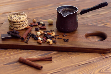 cezve of freshly brewed coffee next to a cakes, nuts on a wooden serving board on a wooden red table