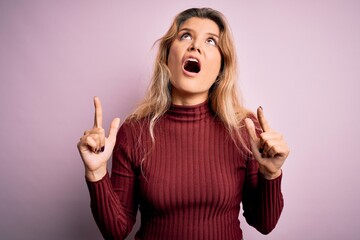 Young beautiful blonde woman wearing casual sweater over isolated pink background amazed and surprised looking up and pointing with fingers and raised arms.