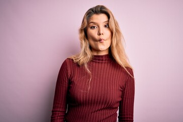 Young beautiful blonde woman wearing casual sweater over isolated pink background making fish face with lips, crazy and comical gesture. Funny expression.