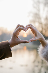 Couples hands are making a heart sign with sun inside