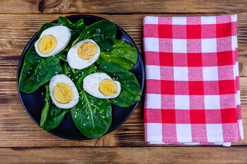 Spinach leaves and halved boiled eggs on a black plate. Top view