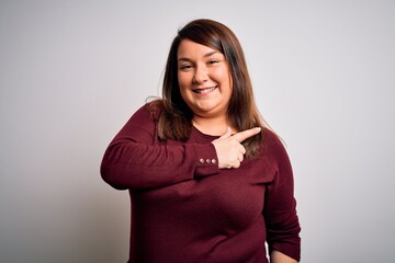 Fototapeta premium Beautiful brunette plus size woman wearing casual sweater over isolated white background cheerful with a smile of face pointing with hand and finger up to the side with happy and natural expression