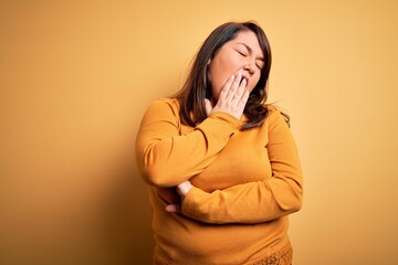 Beautiful brunette plus size woman wearing casual sweater over isolated yellow background bored yawning tired covering mouth with hand. Restless and sleepiness.