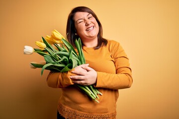 Beautiful plus size woman holding romantic bouquet of natural tulips flowers over yellow background...