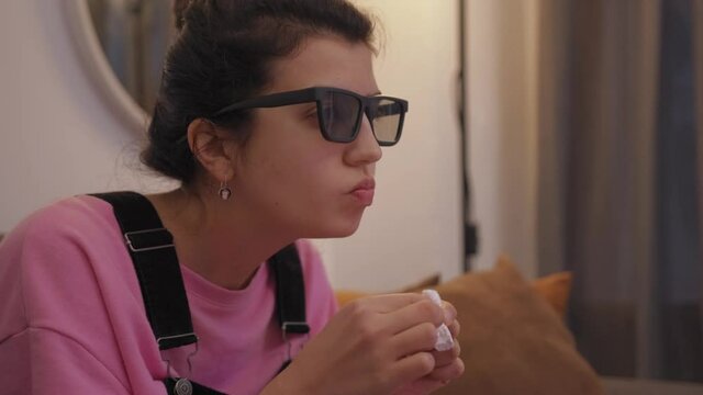 front view of woman in 3d glasses sitting on sofa and eating zefir while watching tv in living room