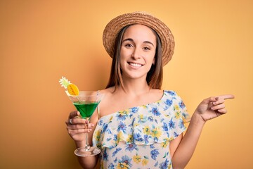 Young beautiful tourist woman on vacation wearing summer hat drinking cocktail beverage very happy pointing with hand and finger to the side