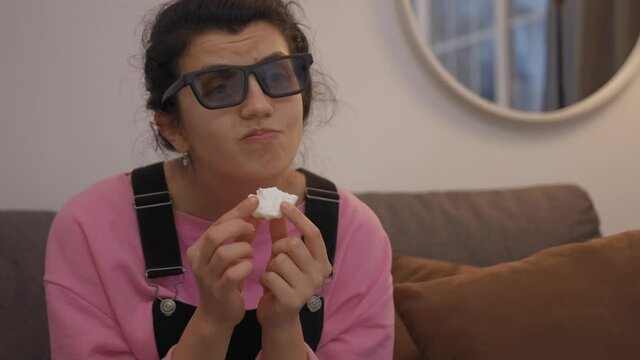 front view of woman in 3d glasses sitting on sofa and eating zefir while watching tv in living room
