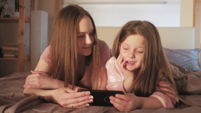 Mother daughter leisure. Home entertainment. Woman little girl watching video on phone in bed.
