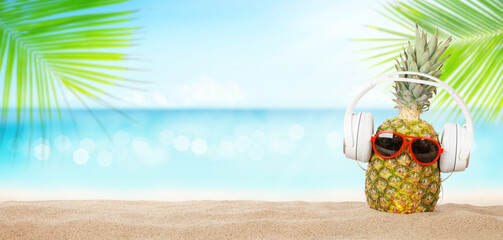 Pineapple with sunglasses and headphones on hot sand beach