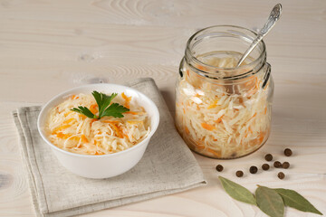 Fermented cabbage with carrots in a glass jar and a white plate.