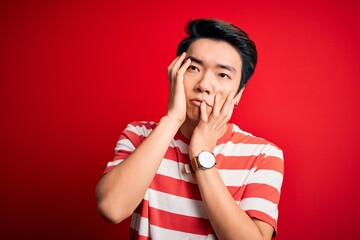 Young handsome chinese man wearing casual striped t-shirt standing over red background Tired hands covering face, depression and sadness, upset and irritated for problem