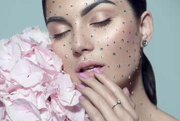 Beauty fashion Woman face decorated with gem stones, crystals. Closeup Portrait with Hydrangea. Model girl with holiday Glamour shiny professional make up with gems, jewellery, jewelry, accessories © Subbotina Anna