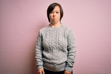 Young down syndrome woman wearing casual sweater over isolated background puffing cheeks with funny face. Mouth inflated with air, crazy expression.