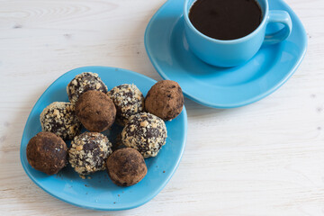 Energy balls on a plate and a Cup of coffee on a white table. Healthy homemade chocolate dessert for Breakfast will fill you with energy . Sprinkle nuts and cocoa