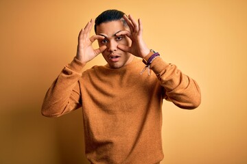 Young brazilian man wearing casual sweater standing over isolated yellow background Trying to open eyes with fingers, sleepy and tired for morning fatigue