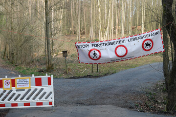 Sperrung von Einfahrt zu Waldgebiet mit Banner und Aufschrift Stop! Forstarbeiten! Lebensgefahr -...