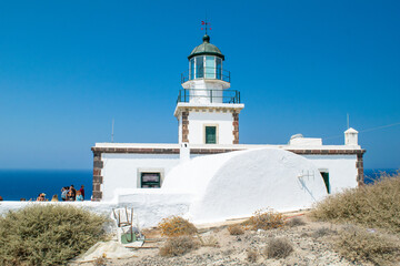 Historic Greek Lighthouse in Akrotiri with a white plastic chair in front of it and tourists at the back