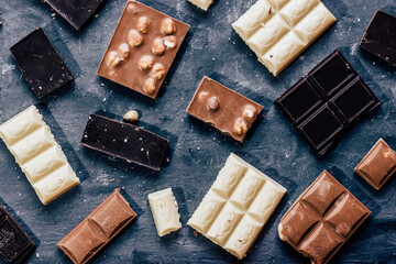 Various chocolate pieces black, milk with nuts and white on a concrete background top view .