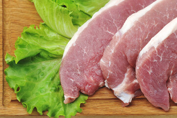 raw pork steak - pork neck - with lettuce leaves on a wooden Board