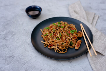 Asian udon noodles with chicken vegetables and teriyaki sauce with chopsticks and a linen napkin on...