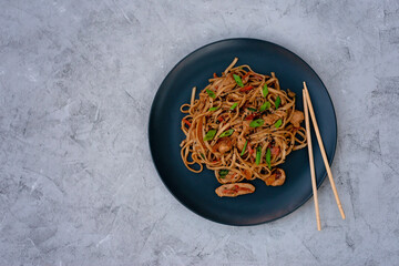 Asian udon noodles with chicken vegetables and teriyaki sauce with chopsticks on a gray concrete background. Chinese and Japanese cuisine. Copy space.