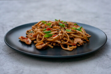 Asian udon noodles with chicken vegetables and teriyaki sauce on a gray concrete background. Chinese and Japanese cuisine.