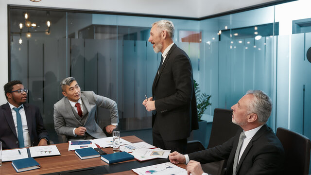 Working together. Confident mature businessman in classic wear discussing new project with his multicultural colleagues