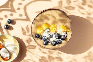 Collagen Powder and Healthy Smoothie from Banana, Pineapple and gluten free oats in the Coconut Shell Bowl, strong shadows. Healthy summer breakfast, top view