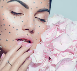 Beauty fashion Woman face decorated with gem stones, crystals. Closeup Portrait with Hydrangea. Model girl with holiday Glamour shiny professional make up with gems, jewellery, jewelry, accessories © Subbotina Anna