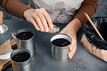 Young woman sowing seeds in metal cans.