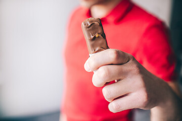 Young man in red shirt isolated over white background. Close up hand holding swet snack. Tasty delicious chocolate bar.