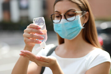 Close up of girl with medical mask using hand sanitizer gel in city street. Antiseptic, Hygiene and Healthcare concept. Focus on hands.