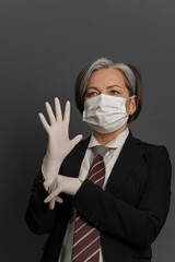 Caucasian Businesswoman in protective mask put on disposable gloves. Mature female office worker...