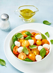 Caprese salad with yellow tomato cherry and mini mozzarella cheese in white bowl on white plate. Bocconcini mozzarella cheese with basil leaves.
