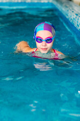 Fototapeta na wymiar Happy girl in pink swimsuit with swimming hat and glasses in the blue pool in sportclub